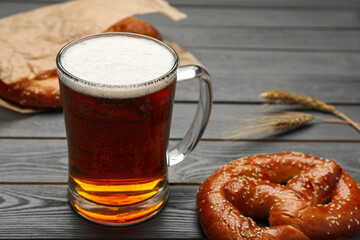 Mug of beer with tasty freshly baked pretzel on grey wooden table, closeup