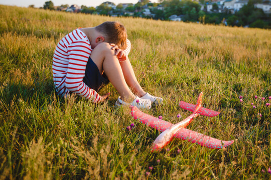 A school-age boy is sad sitting with a broken plane. The concept of broken hopes. - Powered by Adobe
