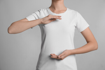 Obraz premium Woman holding hands near chest on light grey background, closeup