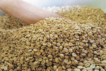 Raw coffee beans in hot pan with wooden paddle