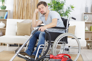 Fototapeta na wymiar borde disabled man in wheelchair uses a vacuum cleaner