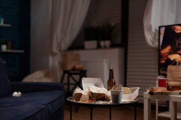 Nobody in living room with messy rubbish cans and leftovers food on table. Empty home space with beer bottles, trash, dirty garbage covered in unhealthy snacks. Stinky unorganized place.