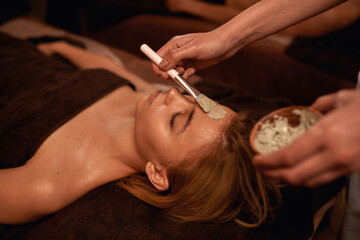 Cosmetician applying clay mask on face of woman