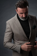 Portrait of a stylish elegant senior businessman with a beard and casual business clothes in photo studio isolated on dark background gesturing with hands