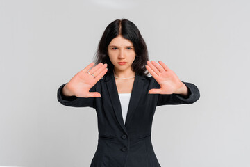 Please, do not, stop. Young serious dark-haired girl, who is looking in the camera and extends palms in stop sign, standing over gray background. Stay home. Social distancing. New normal behavior