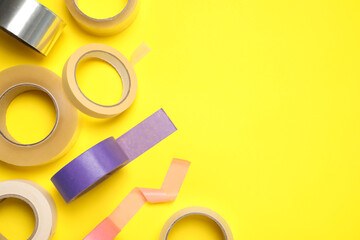 Many rolls of adhesive tape on yellow background, flat lay. Space for text