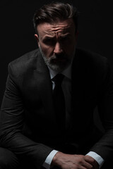 Fototapeta premium Portrait of a stylish elegant senior businessman with a beard and casual business clothes in photo studio isolated on dark background gesturing with hands
