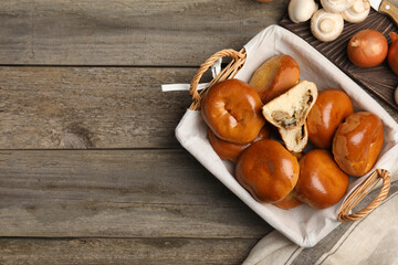 Wicker basket with delicious baked mushrooms and onion pirozhki on wooden table, flat lay. Space for text