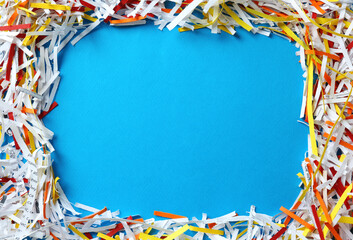 Frame of shredded colorful paper strips on light blue background, flat lay. Space for text