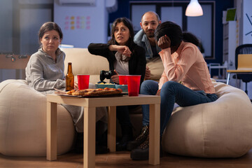 Coworkers feeling frustrated about lost video games play, doing leisure activity at office party after hours. Sad colleagues having fun with technology, beer bottles and pizza at celebration.