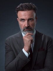 Portrait of a stylish elegant senior businessman with a beard and casual business clothes in photo studio isolated on dark background gesturing with hands
