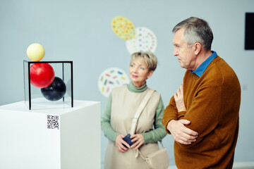 Senior Caucasian man and woman visiting exhibition in museum of modern arts looking at contemporary...