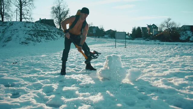 Bodybuilder with a ballon compressed air drager on his back and in a full face mask hits a big tire with a sledgehammer