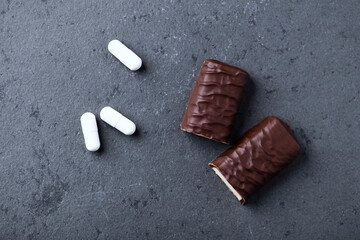 High Protein bar and creatine capsules. Bodybuilding food supplements on dark stone background. Top view. Close up. Copy space. 