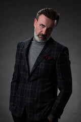 Obraz premium Portrait of a stylish elegant senior businessman with a beard and casual business clothes in photo studio isolated on dark background gesturing with hands