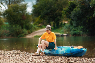 Outdoor activities. A young woman is sitting on a kayak and scratching her leg from a mosquito...