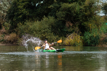 Happy bearded man in shirt and cap kayaking at the river with splashes. Copy space. The concept of watersport