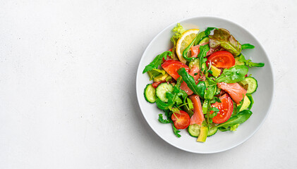 Salad with salmon, vegetables and fresh herbs on a light background.