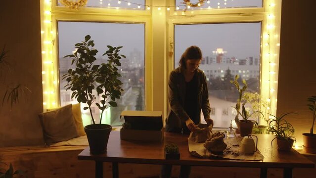 A focused young girl in a beautifully decorated room is packing stabilized moss and replanting houseplants. Slow motion