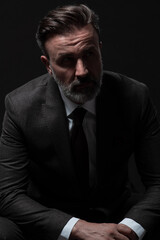 Fototapeta premium Portrait of a stylish elegant senior businessman with a beard and casual business clothes in photo studio isolated on dark background gesturing with hands