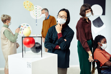 Group of modern diverse multi-ethnic people wearing protective masks looking at contemporary art...