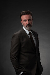 Portrait of a stylish elegant senior businessman with a beard and casual business clothes in photo studio isolated on dark background gesturing with hands