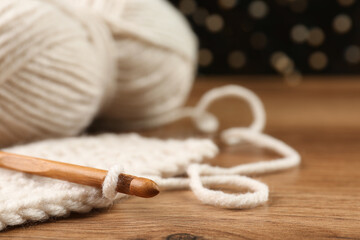Knitting and crochet hook on wooden table against blurred lights, closeup. Space for text