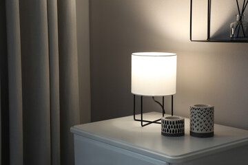 Stylish lamp and candles on white nightstand in room, space for text