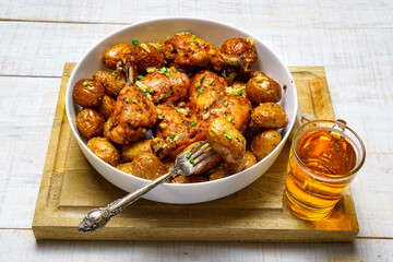 tasty lunch in rural style, healthy food - glass of beer, fried chicken meat and unpeeled roasted potatoes, chopped leeks, cooked food on a white wooden boards