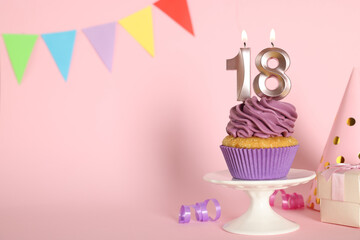 Delicious cupcake with number shaped candles on pink background, space for text. Coming of age party - 18th birthday