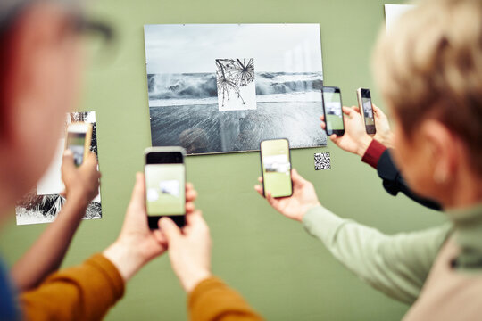 Unrecognizable people scanning QR code using smartphones to get more information about photo on wall at exhibition