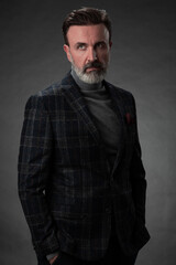 Fototapeta premium Portrait of a stylish elegant senior businessman with a beard and casual business clothes in photo studio isolated on dark background gesturing with hands