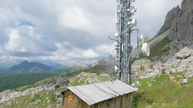 Radio repeater and telephone signal in the high mountains. at the base of the repeater pole a small wooden hut. in the background mountains in a sunny and spring day with a cloudy sky. pan right