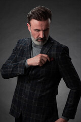 Portrait of a stylish elegant senior businessman with a beard and casual business clothes in photo studio adjusting suit