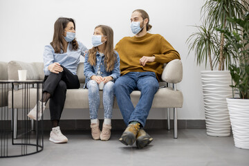 Young family with ten year old girl sitting on a couch at the waiting room of the clinic. Patients...