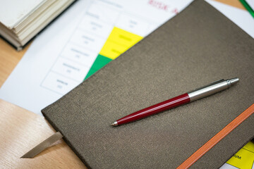 A red luxury ball pen is placed on notebook cover and bulk of document paper sheets. Business and financial working object photo. Selective focus on the pen's part.
