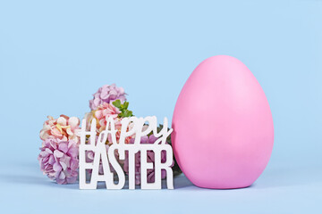 Large pink Easter egg, hydrangea flowers and text 'Happy Easter' on blue background