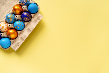 colored golden, blue, light blue Easter eggs on a yellow background for Easter in a tray box
