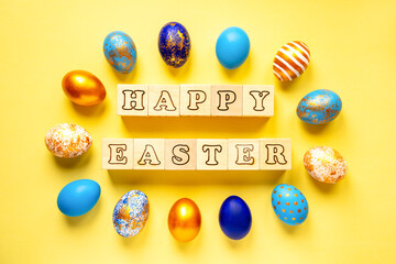 colored golden, blue, light blue easter eggs on a yellow background for easter and a place for text with an inscription from wooden cubes happy easter