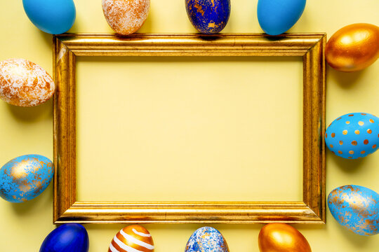 colored golden, blue, light blue Easter eggs on a yellow background for Easter next to a photo frame and a place for text