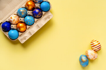 colored golden, blue, light blue Easter eggs on a yellow background for Easter in a tray box