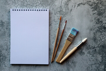 A clean white notebook and brushes on grey background with space to copy.