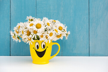 Bouquet of chamomile flowers in funny yellow cup on table. Copy space, front view