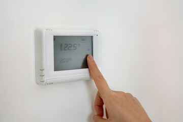 Lowering the temperature for energy saving. Human hand adjusting digital central heating thermostat at home.