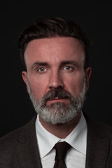 Portrait of a stylish elegant senior businessman with a beard and casual business clothes in photo studio isolated on dark background gesturing with hands