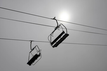 Two chairlift in a very cloudy day with the sun behind the clouds in a very grey day