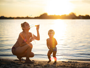 Mom in a bikini plays with the baby blowing bubbles, enjoying the holidays