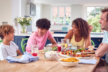 Family Sitting Around Table At Home Eating Meal Together