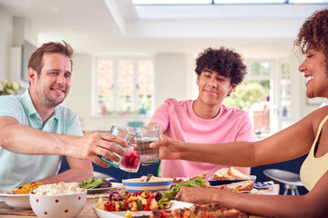 Family With Teenage Son Sitting Around Table At Home Making Toast Before Eating Meal Together