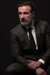 Fototapeta premium Portrait of a stylish elegant senior businessman with a beard and casual business clothes in photo studio isolated on dark background gesturing with hands